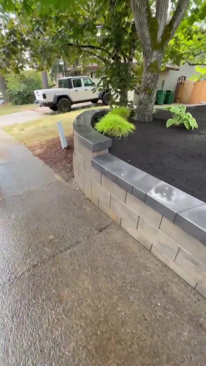 Finished stacked block retaining wall with capstones curving along the sidewalk, planted with ornamental grasses