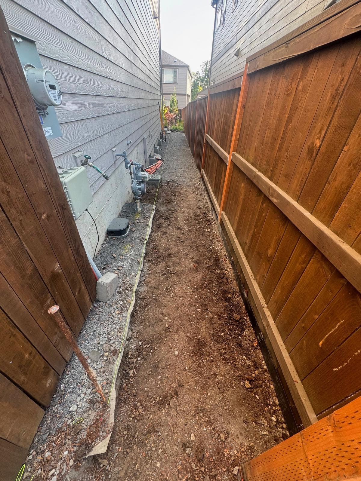Narrow side yard graded and prepped between a house and a new cedar fence